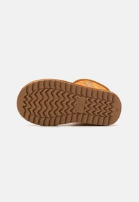 Semelle en caoutchouc marron avec un motif en zigzag, présentant une surface texturée et une marque en relief sur le bord.
