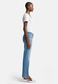 Jeans blu chiaro a gamba dritta con vita media, abbinati a una t-shirt bianca aderente e scarpe con tacco bianche. Tessuto morbido, design classico.