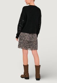 Pull noir en tricot avec des manches à sequins, superposé à une mini-jupe à imprimé léopard, associé à des bottes marron jusqu'aux genoux.