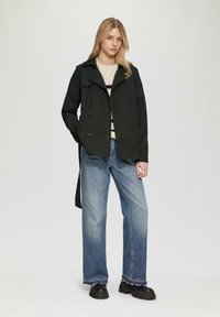 Schwarzer doppelt gelegter Trenchcoat mit Reverskragen, kombiniert mit blauen weit geschnittenen Jeans und klobigen schwarzen Stiefeln.