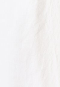 Gładka biała tkanina z delikatnymi zmarszczkami i widoczną teksturą na powierzchni.