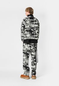 Conjunto de chaqueta y pantalones con un patrón en blanco y negro, fabricado en un tejido texturizado, que presenta un corte relajado y un logo visible en la parte posterior de la chaqueta.