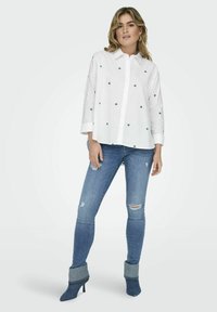 Valge särk roheliste südame mustritega, pikki varrukatega, nööbivarrukaga, koos kulunud siniste teksade ja siniste kontsakingadega, millel on denime aktsendid.