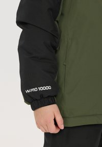 Grön och svart vattentät jacka med elastiska muddars, med "W-PRO 10000" tryck på ärmen, slät textur och sportig design.