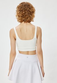 Top corto blanco ajustado con tirantes gruesos, textura suave y espalda redondeada. Combinado con una falda blanca acampanada.
