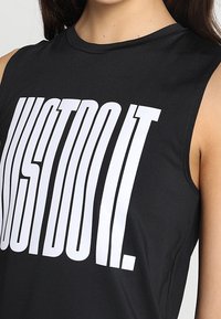 Černý tílko z elastické látky s velkým bílým nápisem „JUST DO IT“ v tučném atletickém písmu. Hladká textura.