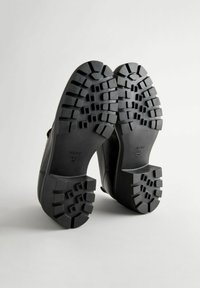 Schwarze Schuhe mit einer strukturierten Gummisohle und tiefen Profilrillen. Glattes Obermaterial mit runder Zehenform. Größe innen angegeben.