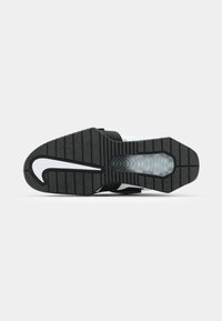 Sandale de sport noire avec semelle en caoutchouc texturé, comportant une section transparente et un accent blanc courbé. Inclut une sangle ajustable.