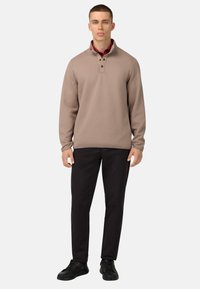 Pullover beige con colletto a mezza zip, tessuto texturizzato, patta con tre bottoni, abbinato a pantaloni neri e sneakers nere.