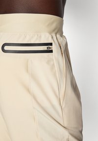 Beige treningsshorts med en tykk midjebånd, med en glidelåslomme med svart trim og glatt tekstur.