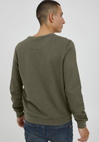 Sudadera verde oliva con cuello redondo, puños y dobladillo acanalados, hecha de un tejido suave. Presenta un diseño sencillo sin patrones ni embellishments.