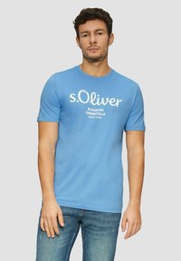 Blue cotton t-shirt with short sleeves, featuring white text that reads "s.Oliver Elevated Essentials Since 1969" on the front.