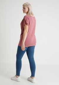 Short-sleeve, relaxed-fit t-shirt in dusty rose, paired with blue skinny jeans and white sneakers, viewed from the back.