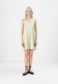 Vestido sem mangas com padrão xadrez verde e decote quadrado, feito de tecido leve; modelo a usar sapatos pretos com atacadores.