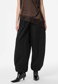 Tumši brūns satīna tops ar mežģīņu apmali, kombineēts ar vaļīgām melnām biksēm. Valkāts ar melniem lakādas zābakiem ar smailiem galiem.