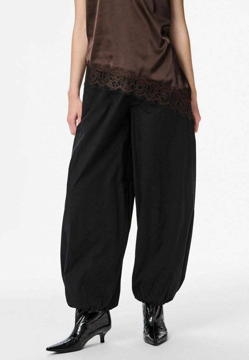 Tumši brūns satīna tops ar mežģīņu apmali, kombineēts ar vaļīgām melnām biksēm. Valkāts ar melniem lakādas zābakiem ar smailiem galiem.