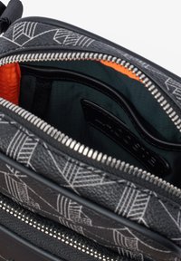 Black zippered bag with geometric white patterns; interior features orange and green lining with black branding label. Textured exterior.