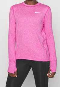 Pitkähihainen urheilupaita kirkkaan pinkkinä, pyöreällä pääntiellä, peukalorei'illä hihoissa ja valkoisella Nike-logolla rinnassa.