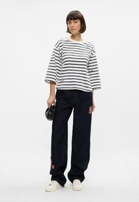 Ριγέ, μακρυμάνικη μπλούζα σε λευκό και ναυτικό μπλε; χαλαρά σκούρα τζιν με λουλουδάτη κεντητική; λευκά αθλητικά παπούτσια; μαύρη τσάντα.