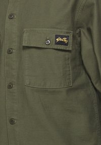 Chemise boutonnée vert olive avec poche à rabat devant ornée d'une étiquette noire et jaune "Stan Ray".