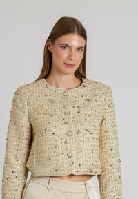 Beige Cropped-Jacke aus strukturiertem Stoff mit Pailletten, mit runder Halslinie, Knopfverschluss und zwei Vordertaschen mit Paspel.