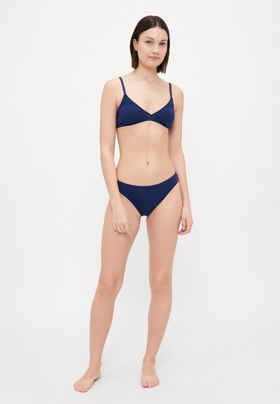 Mornarska bikini komplet, ki vključuje trikotno braletko z nastavljivimi naramnicami in ujemajoče se nizke hlačke, oboje z valovitimi robovi.