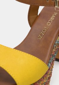 Κίτρινο δερμάτινο σανδάλι με καφέ σχέδιο από φούτερ δέρμα και υφαντή πολύχρωμη βάση με υφή. Χρυσά γράμματα στην εσωτερική σόλα.