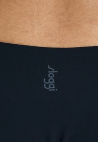 Crne rastezljive gaćice s mekom teksturom, s diskretnim srebrnim logotipom "sloggi 99" na pojasu. Glatki i bezšavni dizajn.
