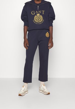 Felpa blu navy con maniche oversize e dettaglio del logo dorato, abbinata a pantaloni da tuta blu navy con branding ricamato. Sneakers incluse.