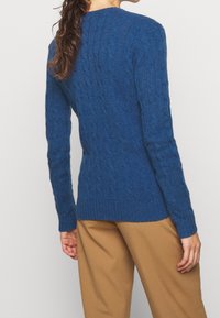 Cable-knit sweater in a deep blue color, featuring a ribbed hem and cuffs. The design showcases a textured pattern throughout.