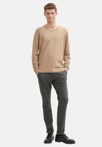 Suéter beige de cuello en V combinado con pantalones sastre gris oscuro y zapatos negros de cordones. Textura suave, diseño ajustado y silueta recta en las piernas.