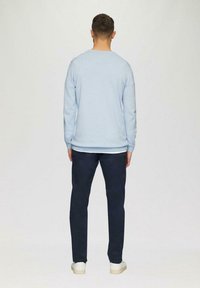 Hellblauer Pullover mit langen Ärmeln und Rundhalsausschnitt, kombiniert mit dunkelblauen Hosen. Das Outfit wird mit weißen Schuhen abgerundet.