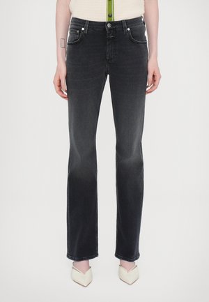 Kobieta ubrana w czarne dżinsy o prostych nogawkach z zapięciem na guzik i suwak, w połączeniu z białymi szpilkami z noskiem w szpic.