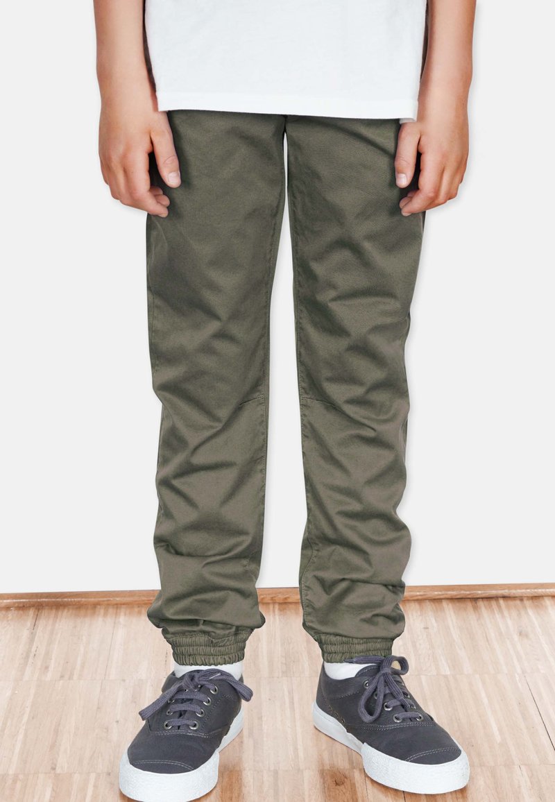 Olivgröna tapered byxor med elastiska muddar, tillverkade av mjukt tyg. Matchade med mörka sneakers med vita sulor och snören.