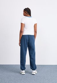 Camiseta blanca de manga corta con un cuello azul, combinada con pantalones de chándal sueltos de color azul marino. El conjunto tiene un ajuste casual y relajado.