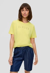 T-shirt jaune à manches courtes avec le texte "LOVELY" en lettres en relief, associé à un short en denim foncé avec une taille élastique et un cordon de serrage.