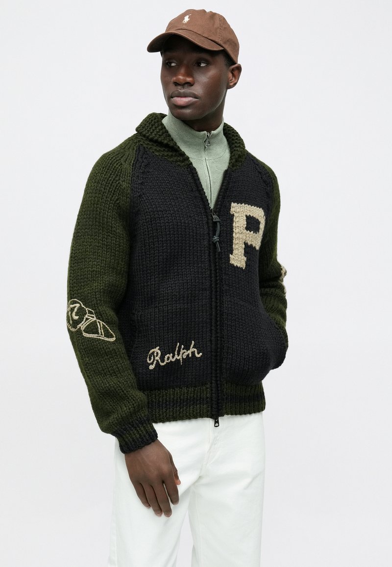 Veste zippée tricotée en vert foncé et noir, avec un "P" brodé et le détail "Ralph", tissu texturé et rayures contrastantes.