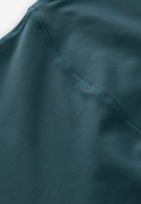 Zacht, donker teal stof met een gladde textuur, voorzien van vlakke naden en een subtiele glans, ontworpen voor comfort en elasticiteit.