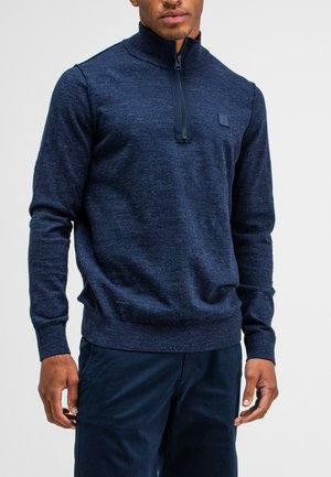 Marineblauwe half-zip trui van textuurgebreid materiaal. Voorzien van een hoge kraag, aansluitende manchetten en een subtiele logo op de borst.