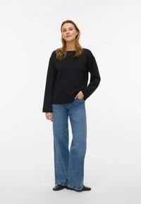 Melna garroku džemperis ar brīvu piegriezumu, kombinēts ar gaiši ziliem plašām biksēm un melniem apaviem. Gluda auduma, minimālistisks dizains.