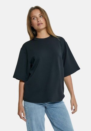 Black oversized t-shirt made of cotton blend, featuring a wide crew neck, short sleeves, and a relaxed fit. Pairing with light blue jeans.