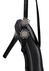Sandale noire à talons hauts avec une finition brillante, présentant deux embellissements en rayons de soleil argentés ornés de strass sur des brides réglables.