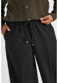 Schwarz, weite Hose mit elastischem Bund und Kordelzug. Glatte Textur, mit silbernen Spitzen an den Kordelzügen.