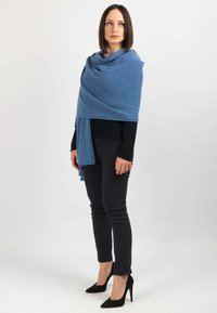 Lyseblå sjal lavet af blødt materiale, draperet over en sort langærmet toppen, parret med sorte skinny jeans og spidse højhælede sko.