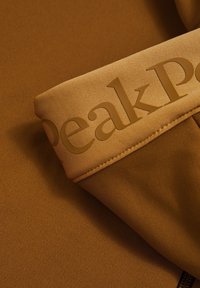 Tessuto marrone con una texture a coste e un logo audace in rilievo di un marrone chiaro contrastante sul polsino, che mette in mostra un design elegante.