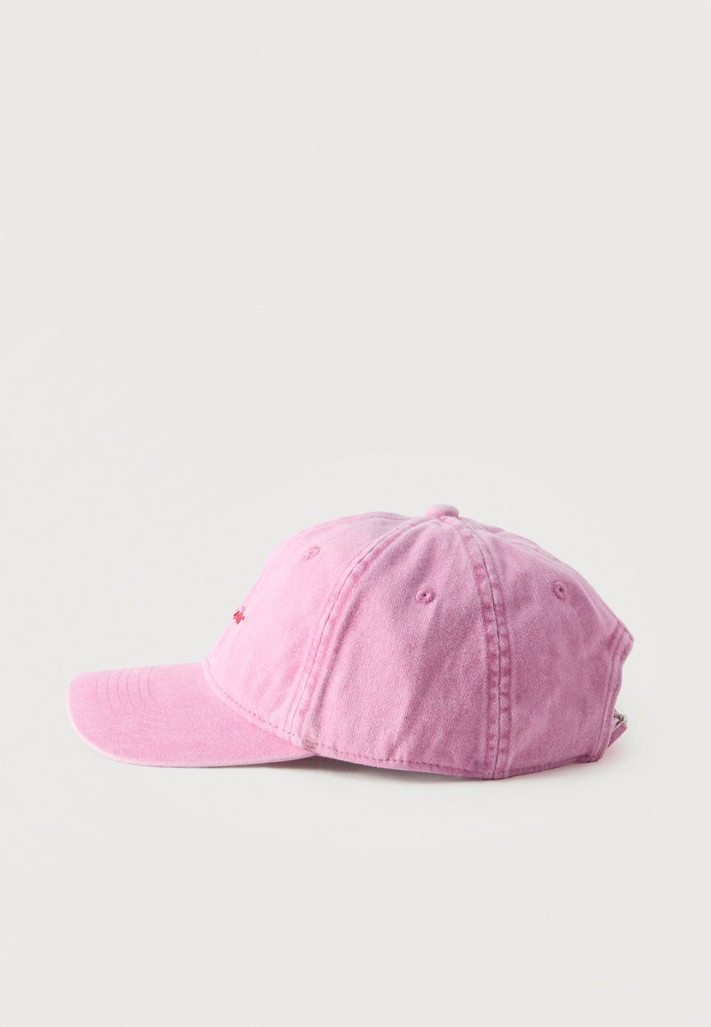 Lyserød cotton baseball cap med buet skygge og syninger på paneler, set fra siden på en ensfarvet lys baggrund.
