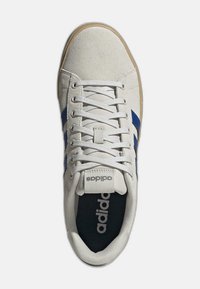 Sneaker bianca in suede con strisce blu, lacci bianchi piatti e una soletta nera con il logo "adidas". Design classico, modello low-top.