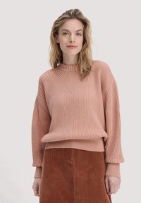 Rippstrick-Sweatshirt in zartem Rosa mit hohem Kragen und Ballonärmeln, kombiniert mit einem strukturierten braunen Cordrock.