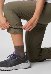 Maslinasto zelene, lagane hlače do koljena s mogućnošću podizanja osigurane kopčom. Uparene s sivim sportskim cipelama i smešnim pletenim čarapama.