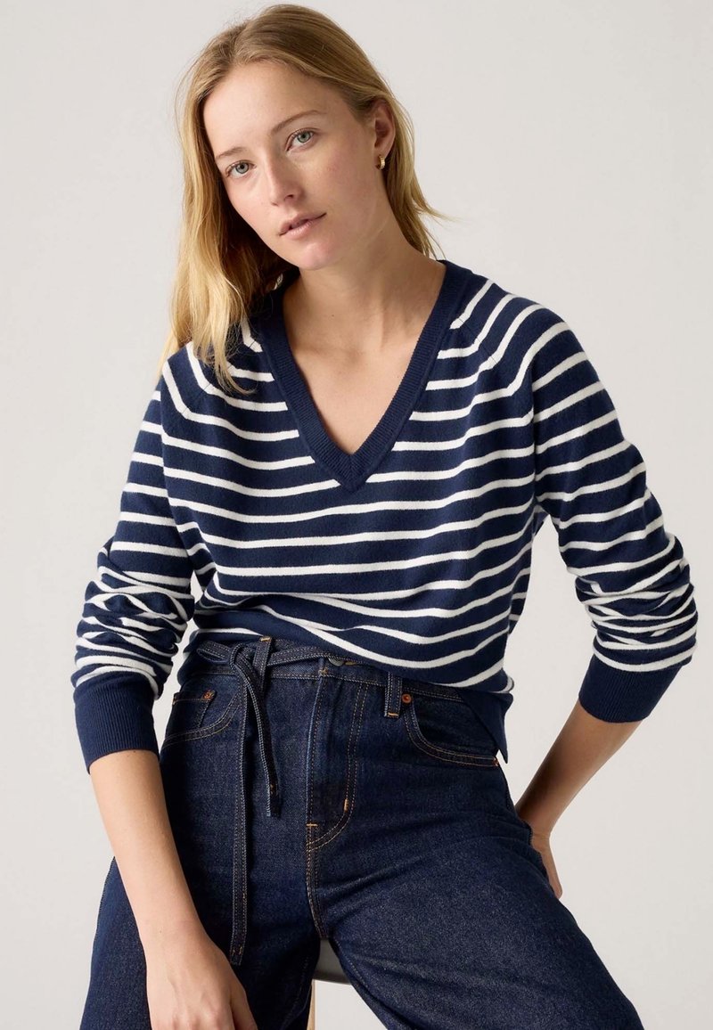 Maglione a righe blu navy e bianche con scollo a V, maniche lunghe e polsini a coste, abbinato a jeans scuri a vita alta.